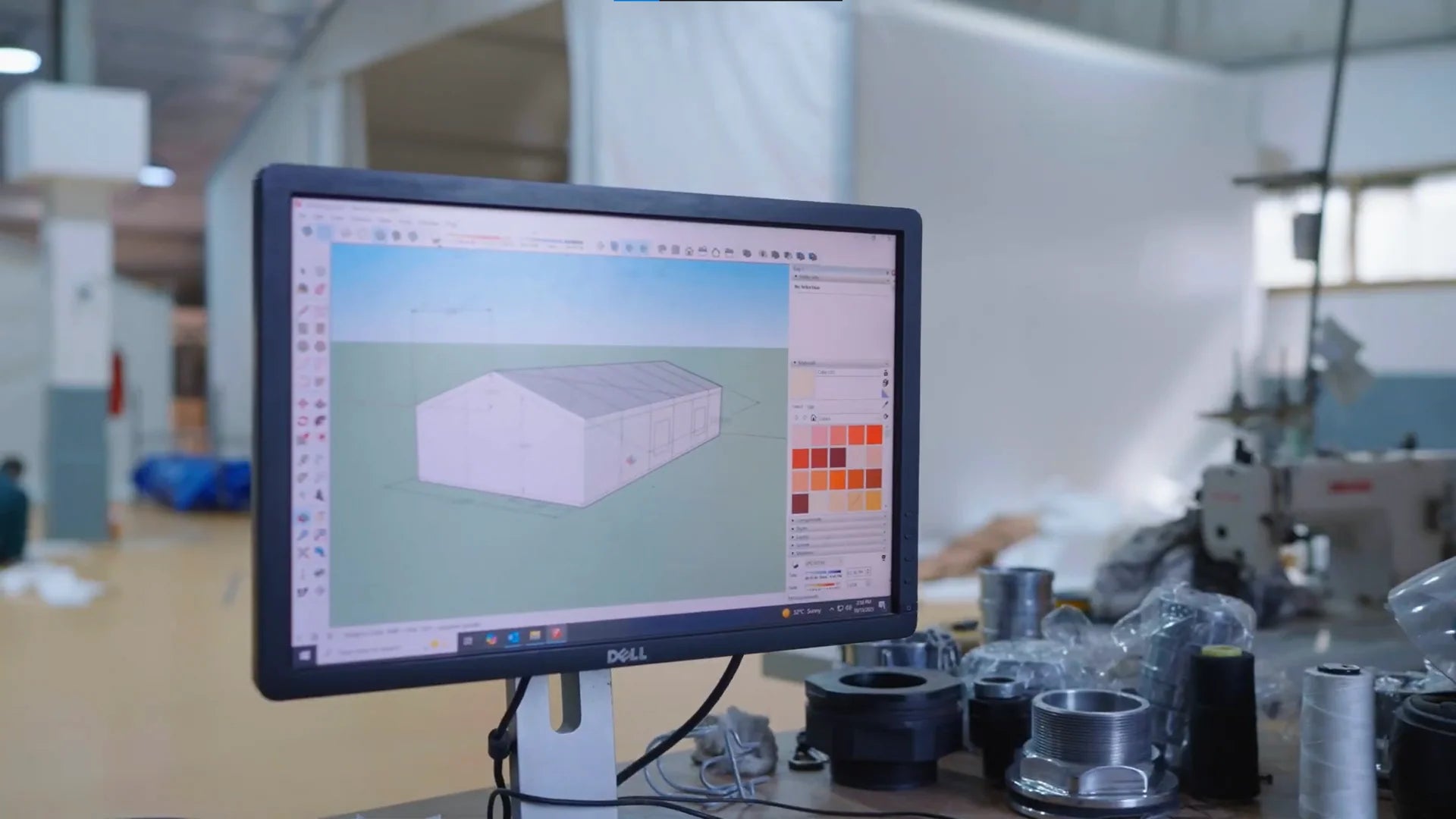 Computer monitor displaying 3D modeling software with a building model on a workshop background